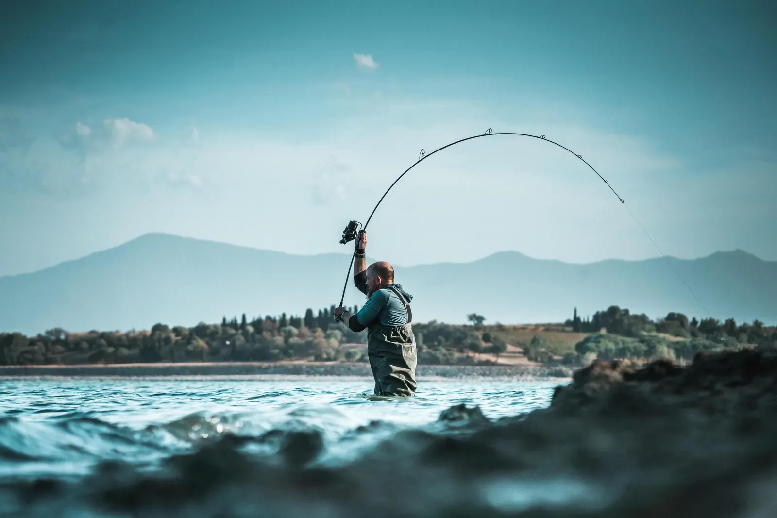 Angler with a bent rod standing in water off rocks
