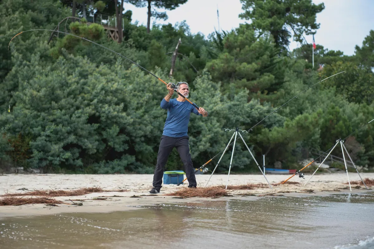 Angler casting a rod from a quiet sandy beach backed by pine trees