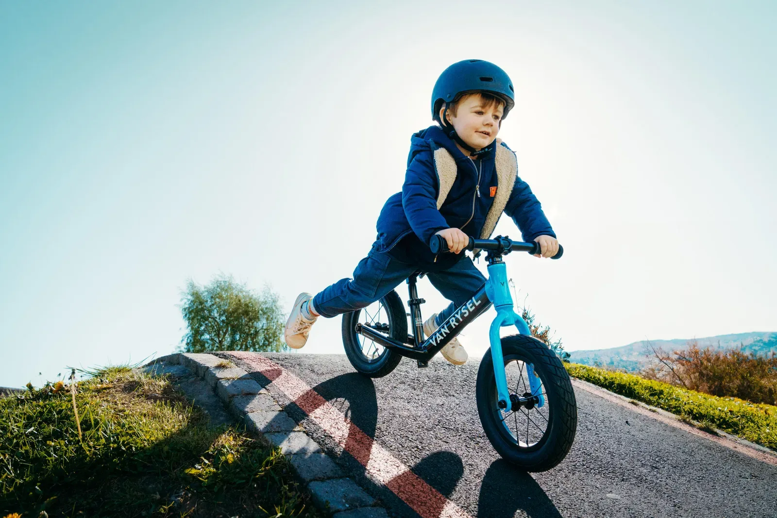 Young boy in a helmet riding a balance bike over a small bump on an outdoor track