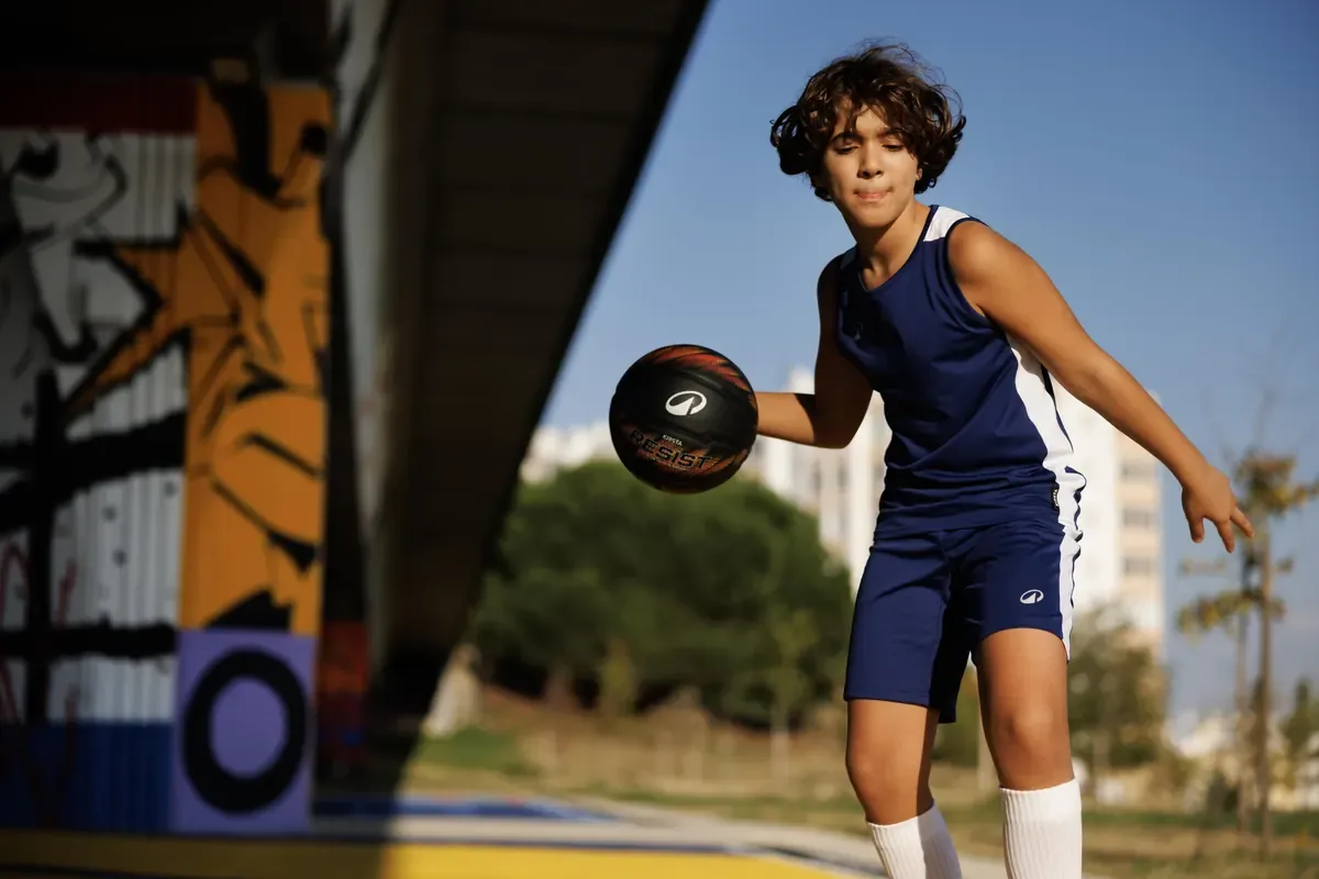 Young player dribbling a basketball on an outdoor court beside a painted mural wall
