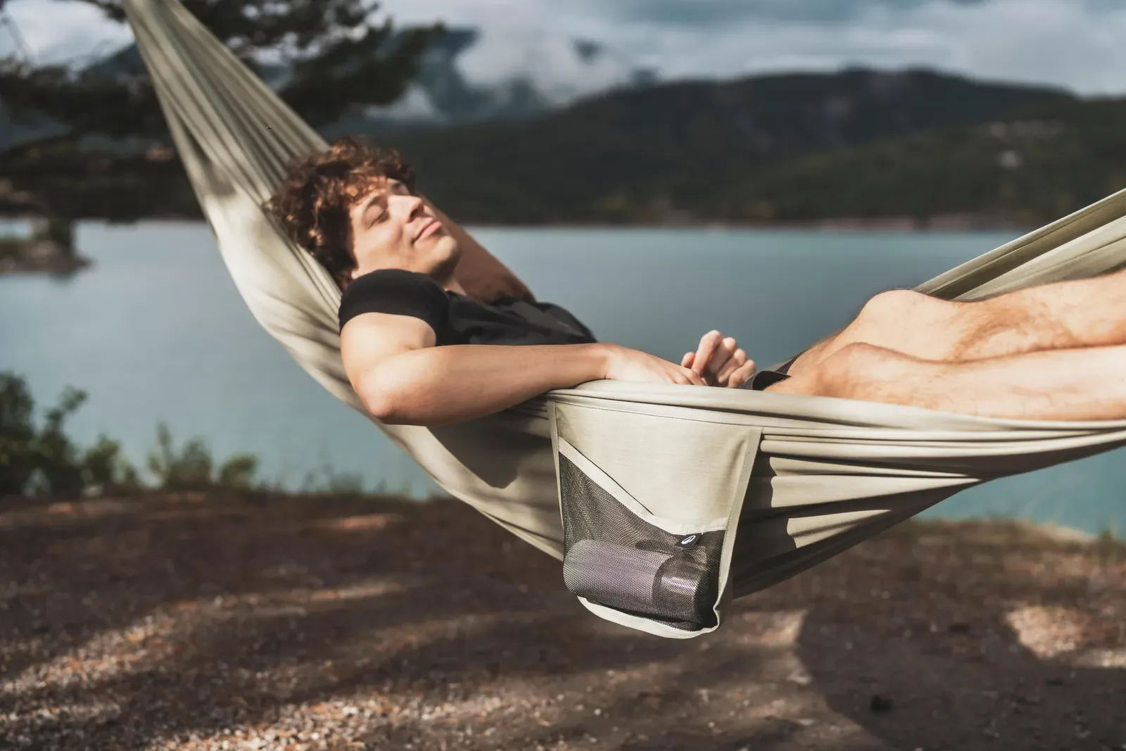 Man relaxing in a hammock strung between trees on a lakeshore