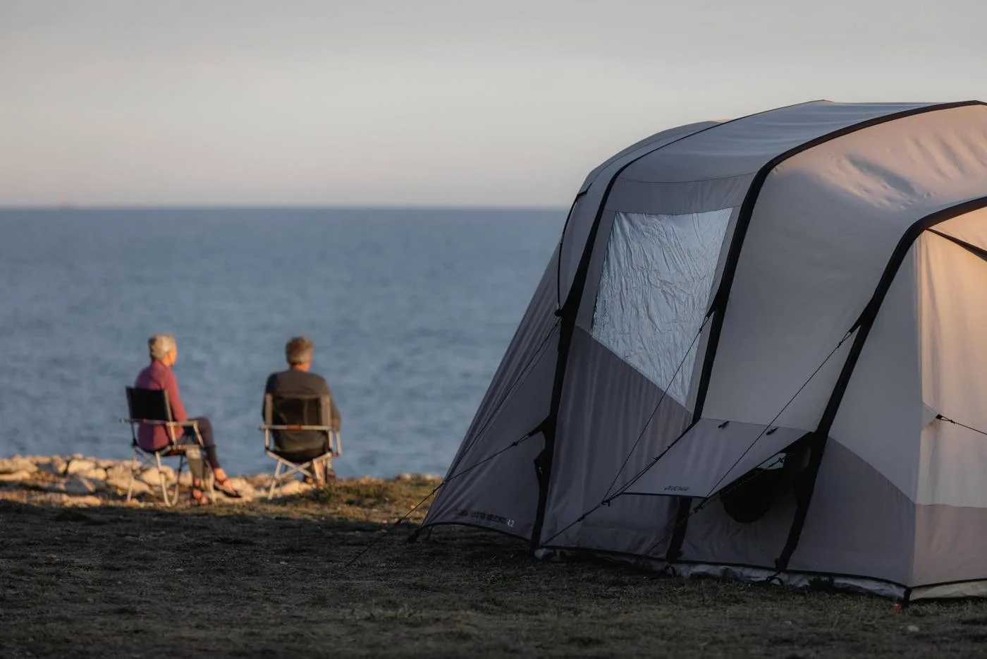 Coastal tent at sunset with campers looking out to sea
