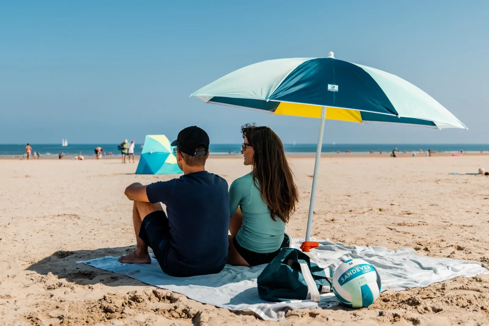 Couple sitting on a beach towel under a beach umbrella looking out to sea