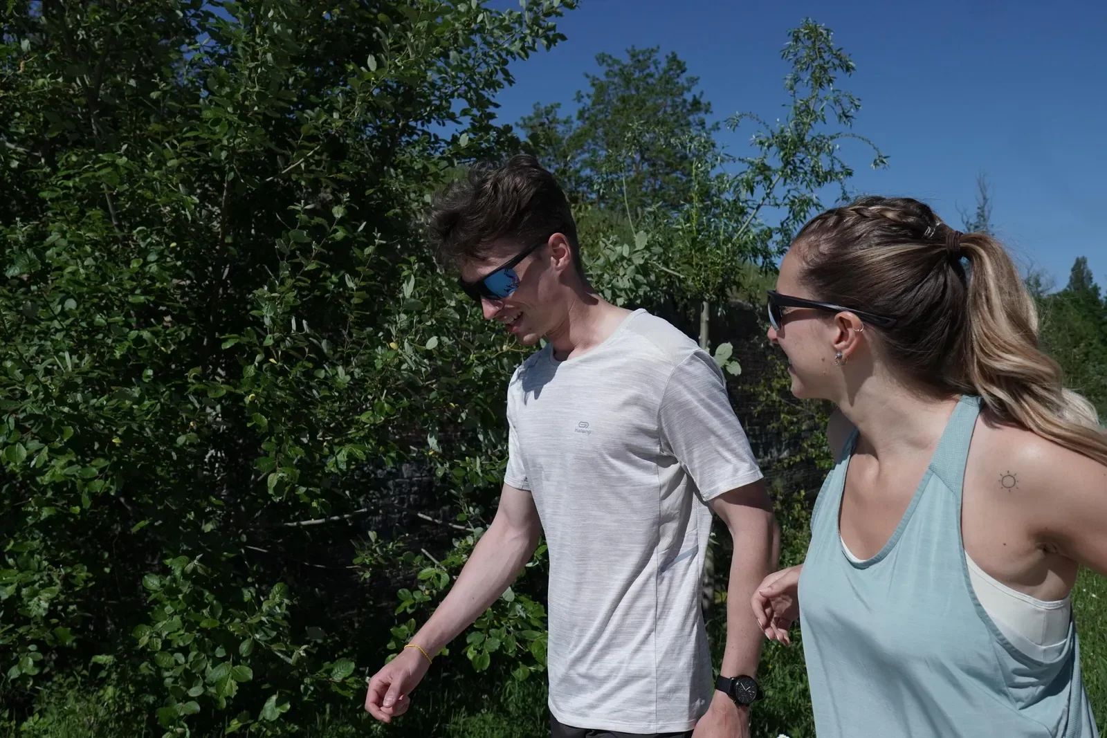 Man and woman in sunglasses walking briskly together on a sunny park trail