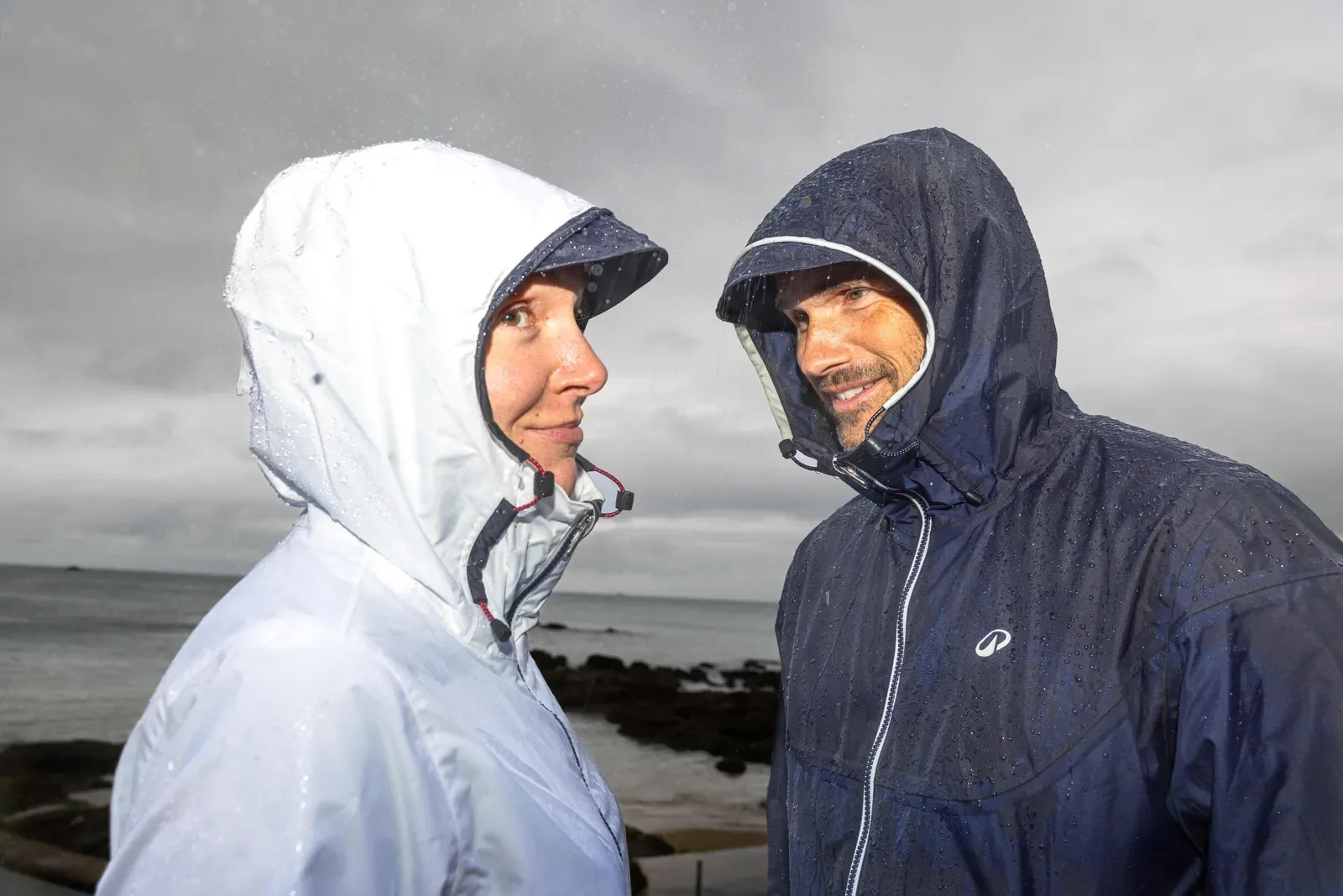Couple in hooded rain jackets on a wet, windy day beside a rocky shoreline