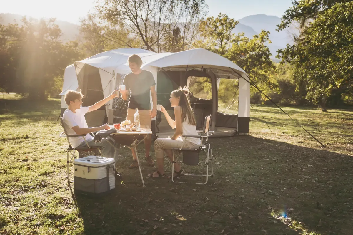 Family sharing drinks around a camp table in front of a large tent on a sunny grassy campsite