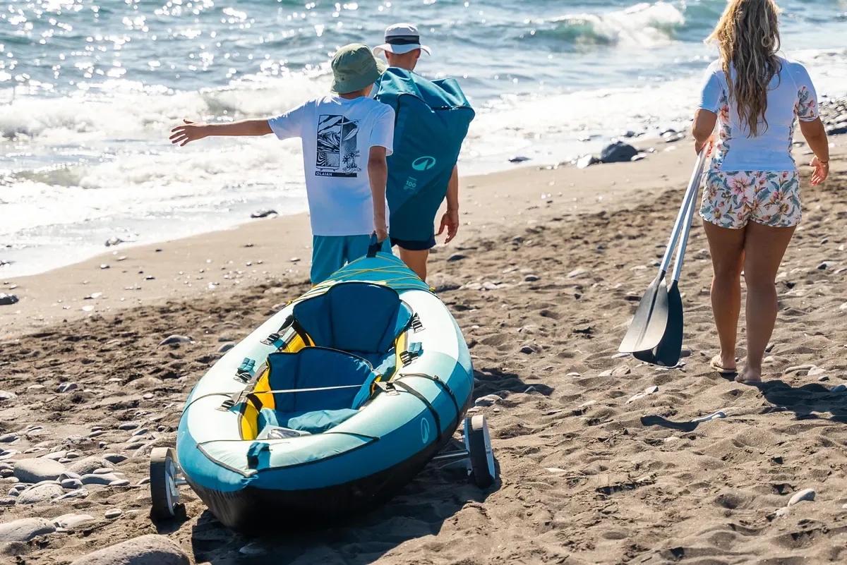 Family wheeling an inflatable kayak along a sandy beach towards the waves