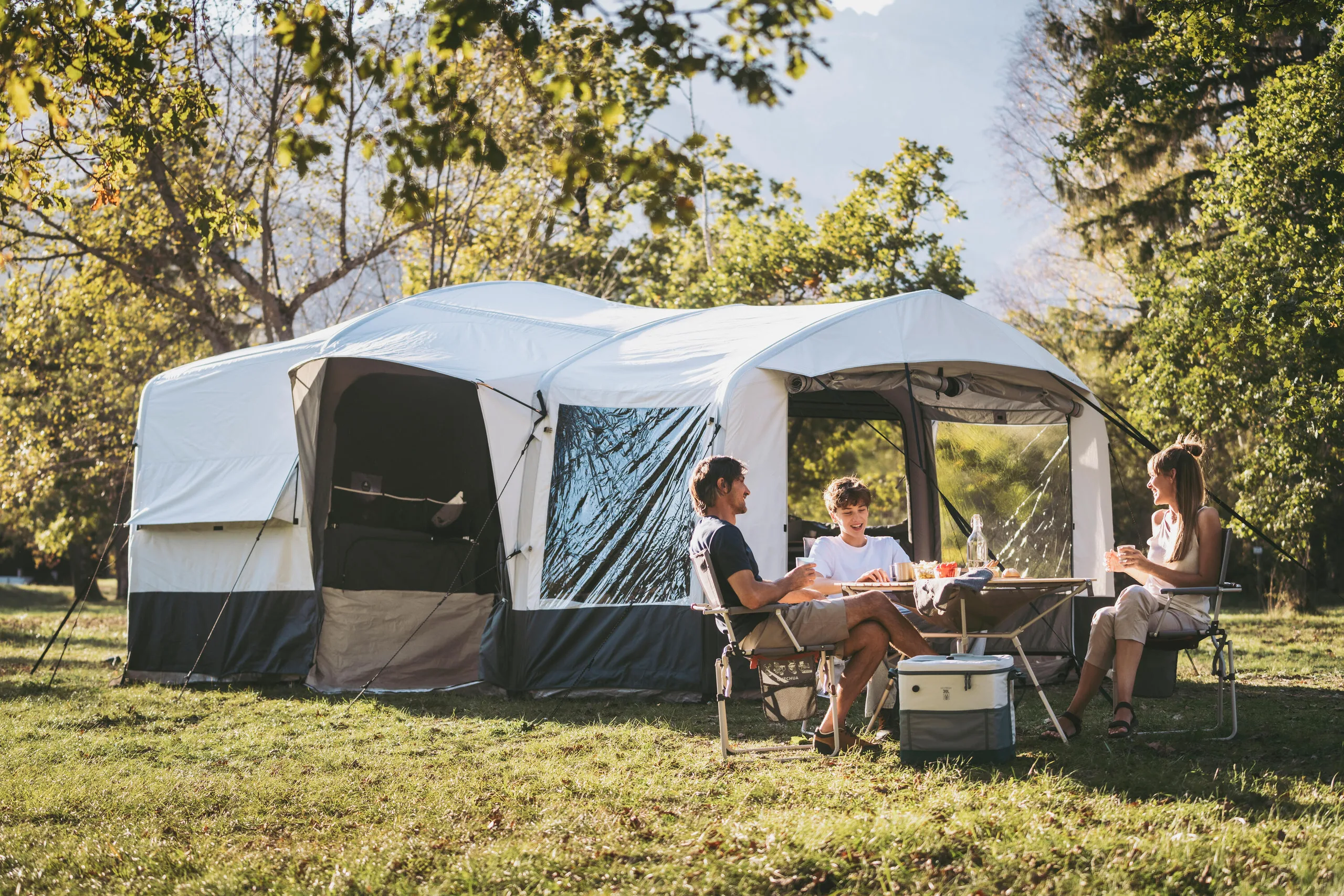 Family eating lunch at a camp table beside a cooler in front of a large tent