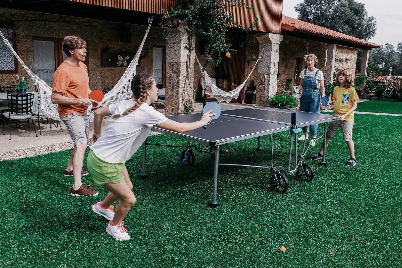 Family playing table tennis on an outdoor table in their backyard