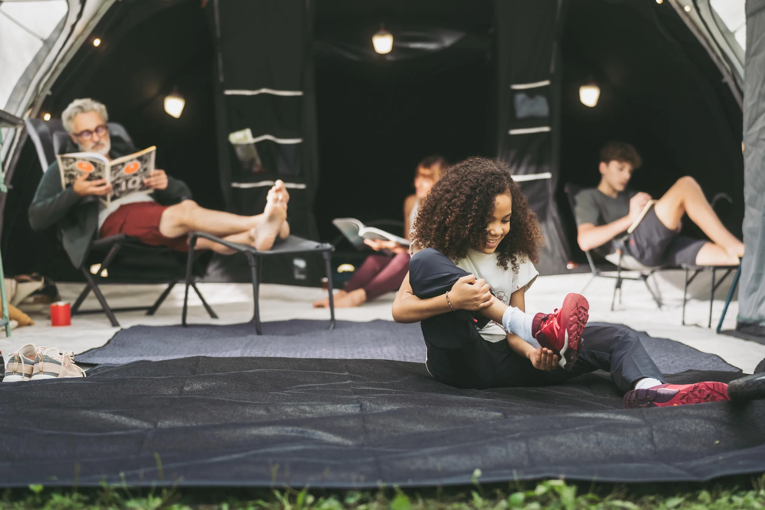 Family relaxing on camp chairs and a rug inside a roomy tent living area