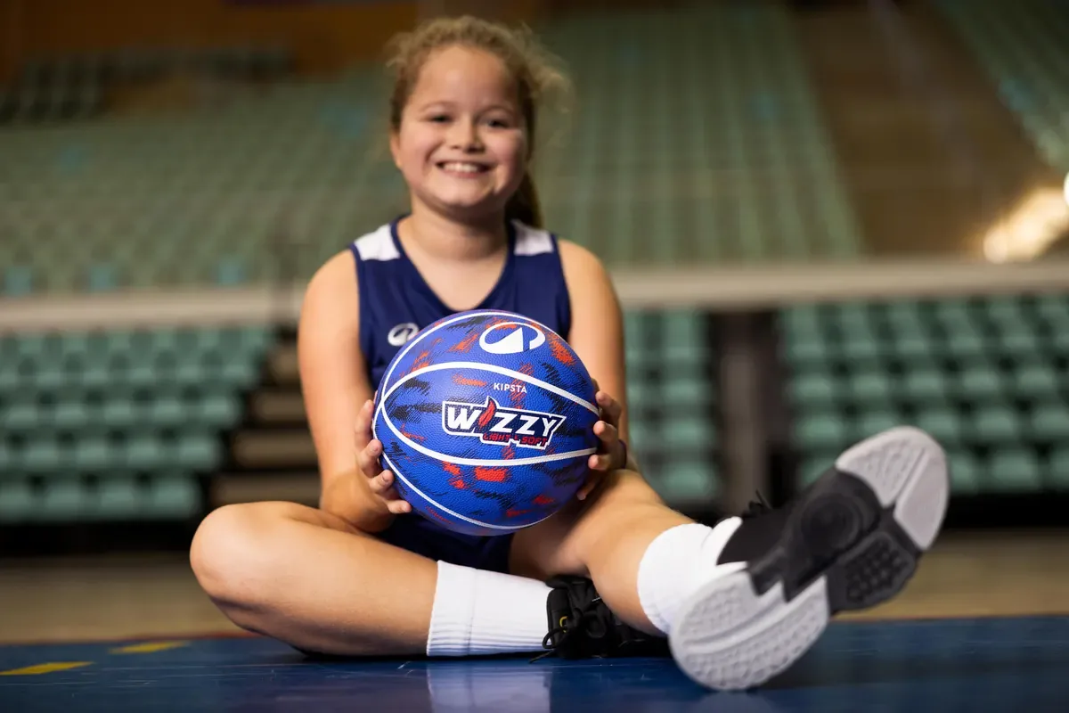 Smiling girl sitting on a court holding a colourful blue kids basketball