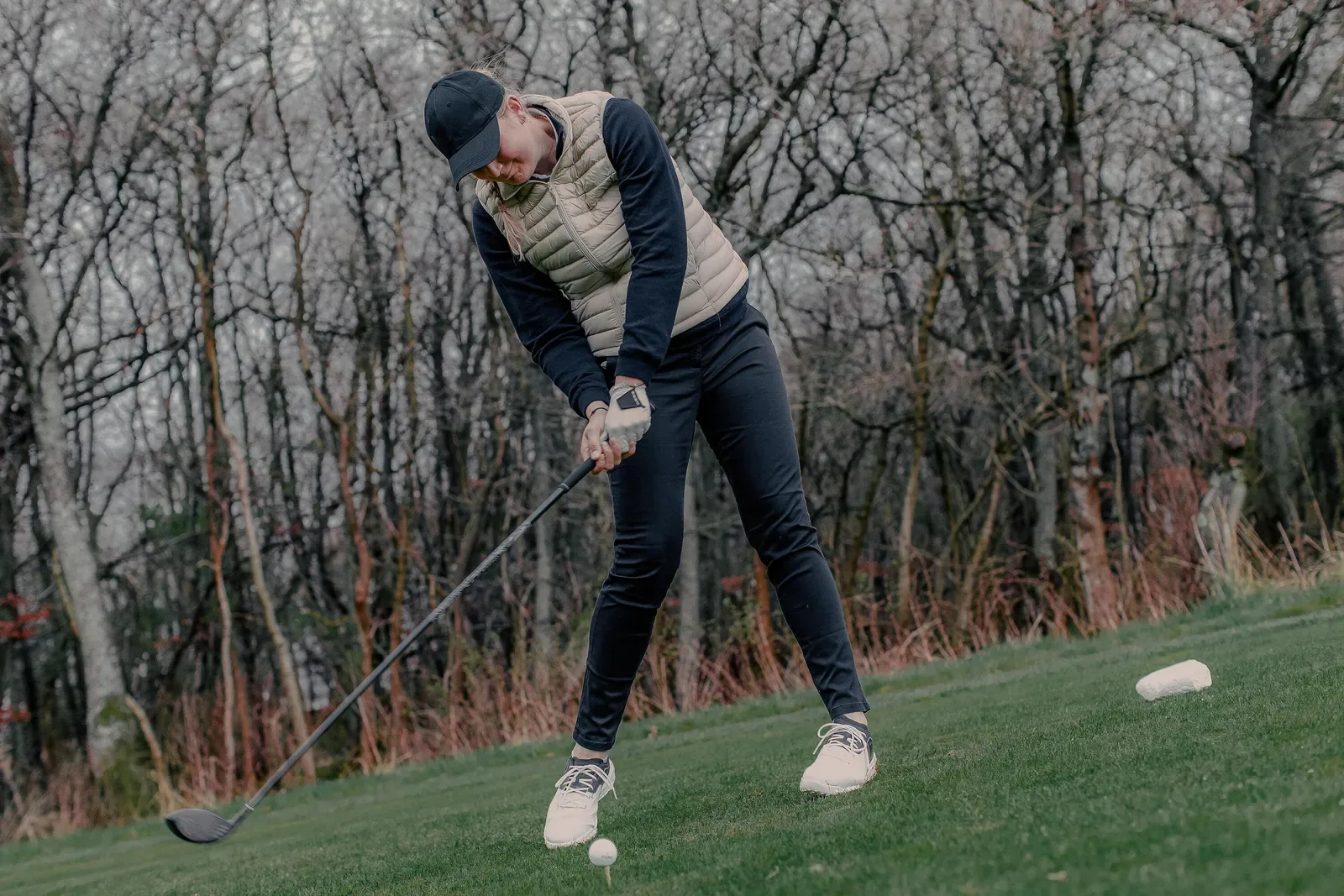 Golfer driving a ball off a tee beside bare trees