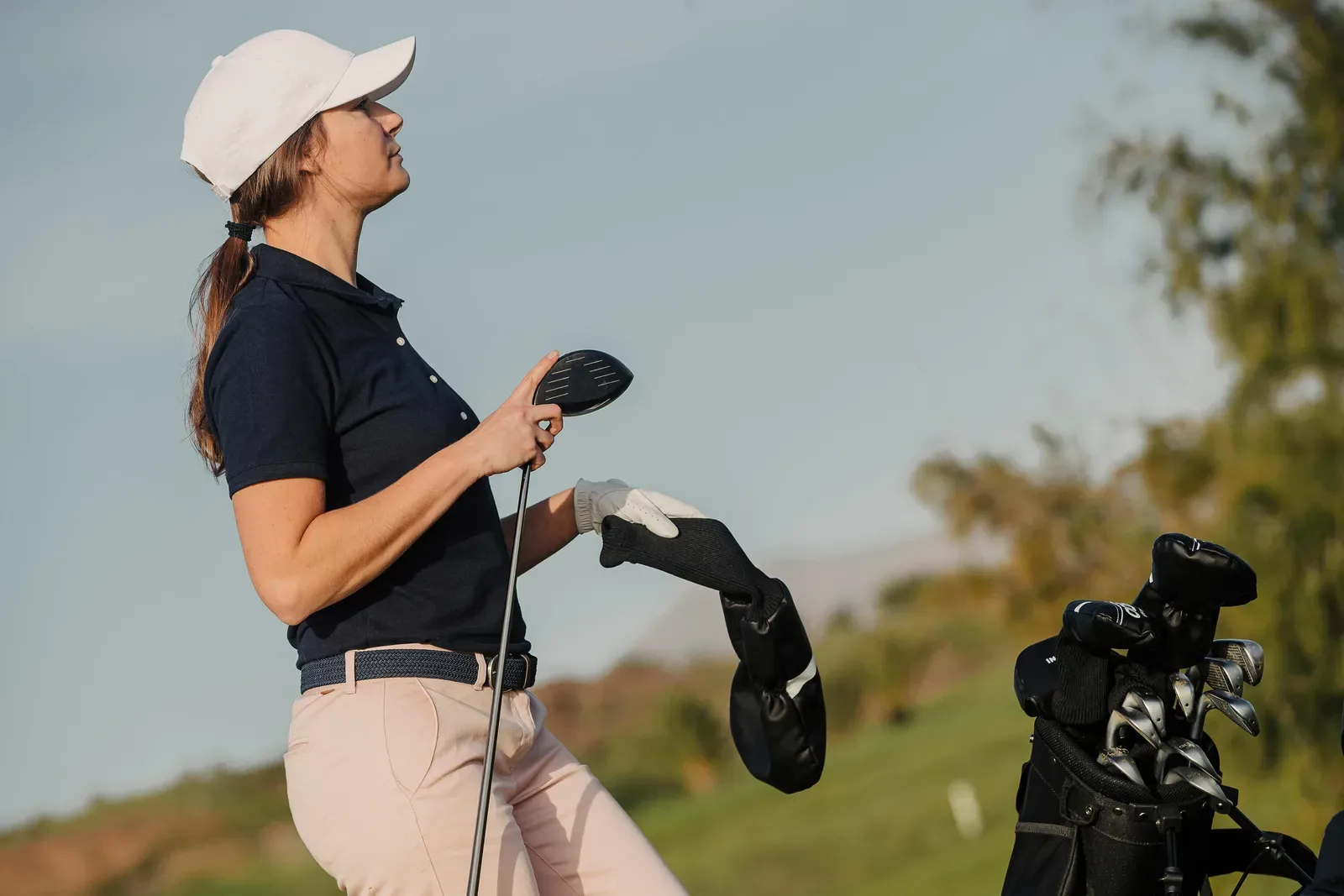 Golfer taking a driver from her bag on a hillside course