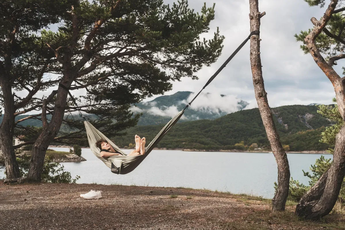 Camper relaxing in a hammock strung between trees beside a calm lake