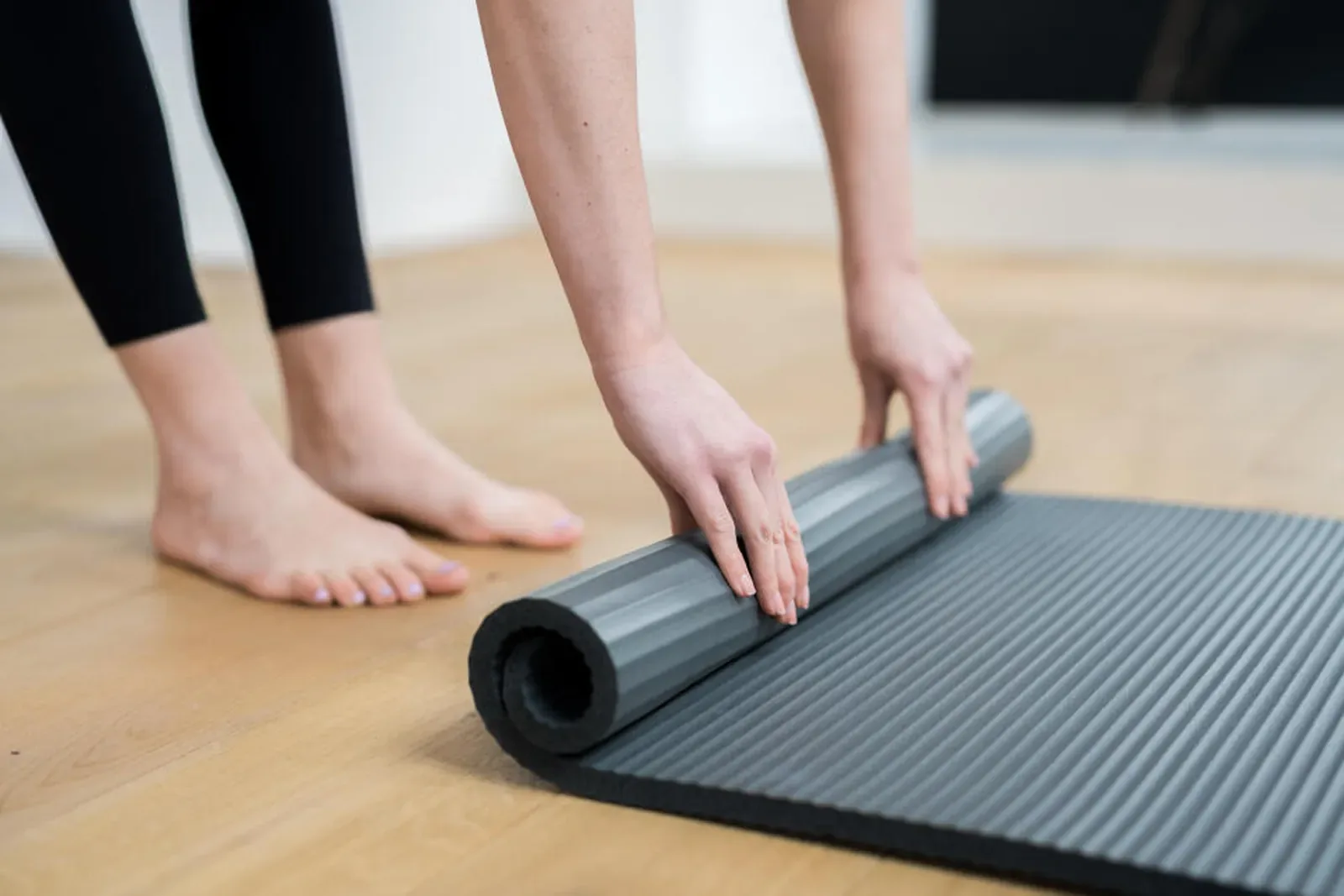 Hands unrolling an exercise mat on a timber floor ready for a workout