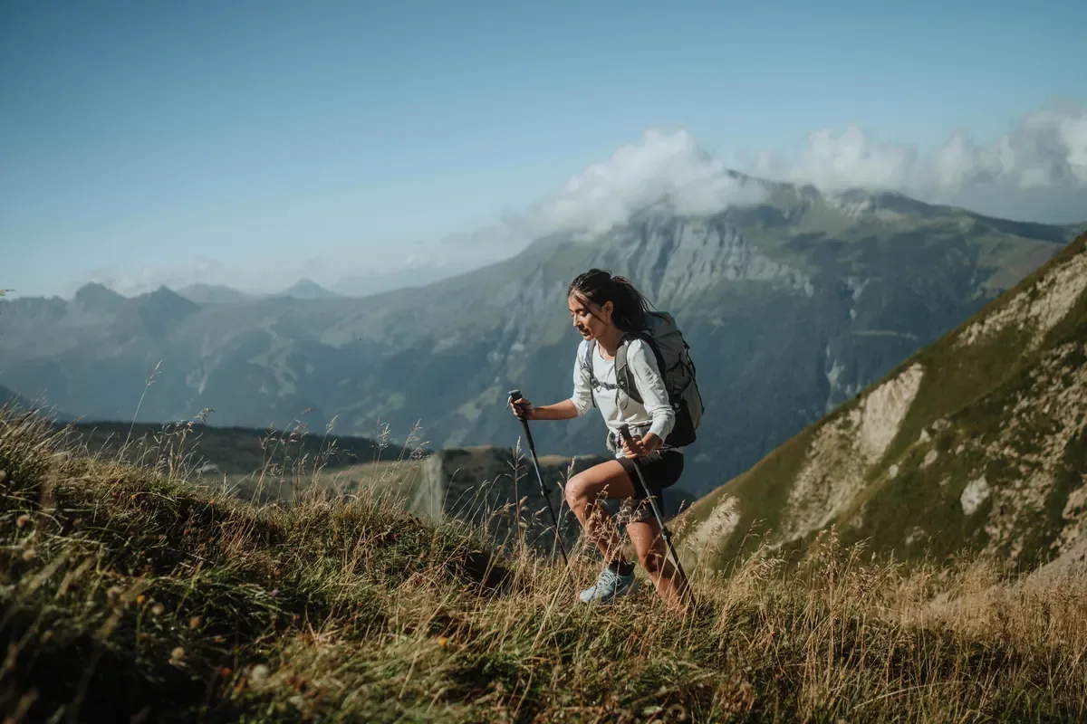 Hiker with trekking poles climbing a grassy ridge above a wide valley