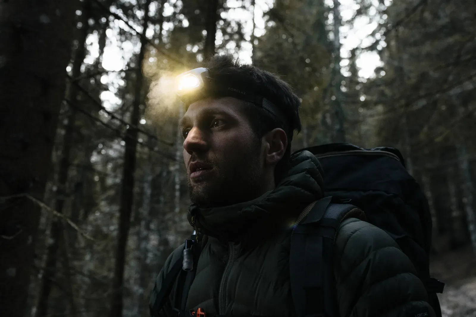 Hiker with a backpack and head torch in a tall, dim forest