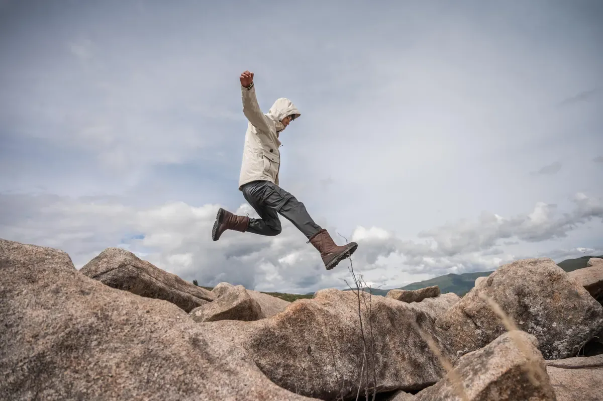 Hiker leaping between large granite boulders under a cloudy sky