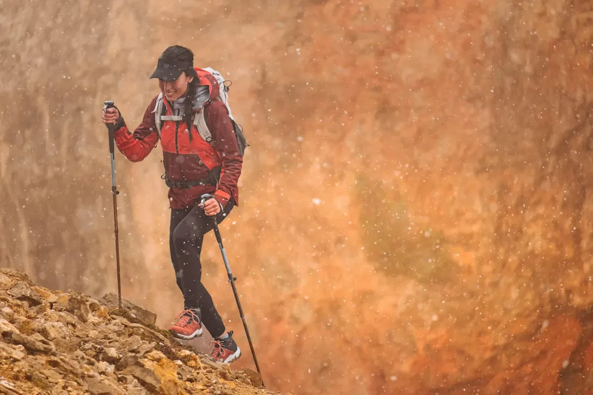 Hiker with trekking poles walking past a weathered red rock face