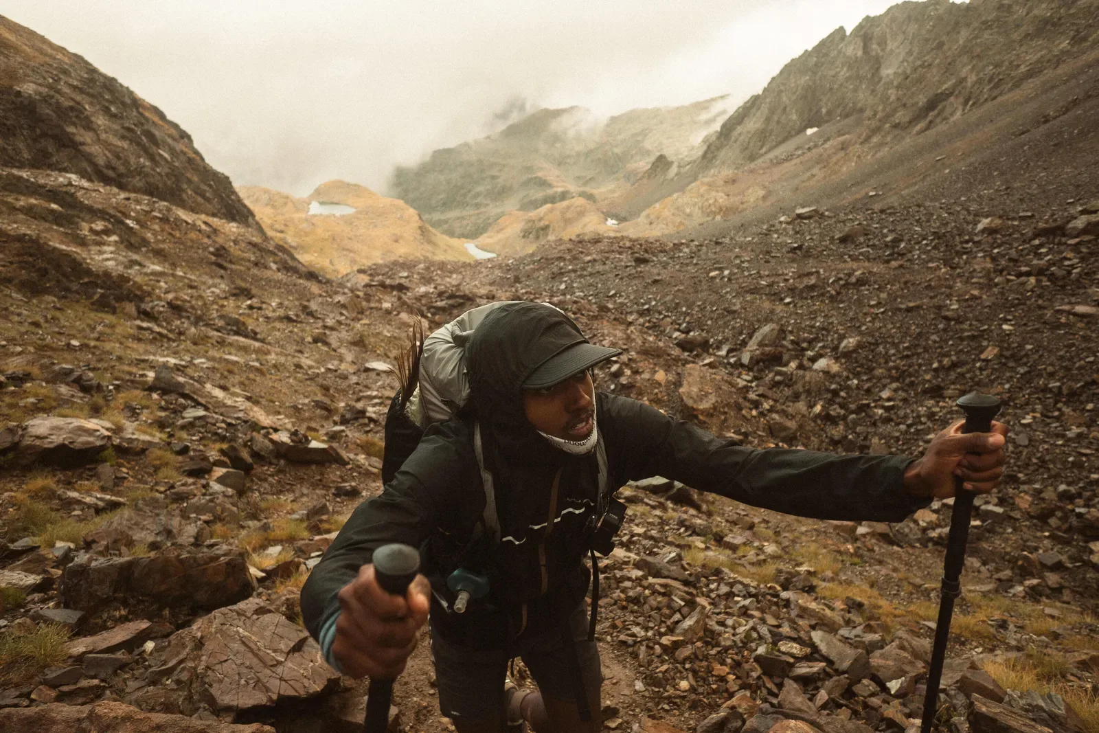 Hiker with trekking poles climbing a rocky track in a misty mountain valley