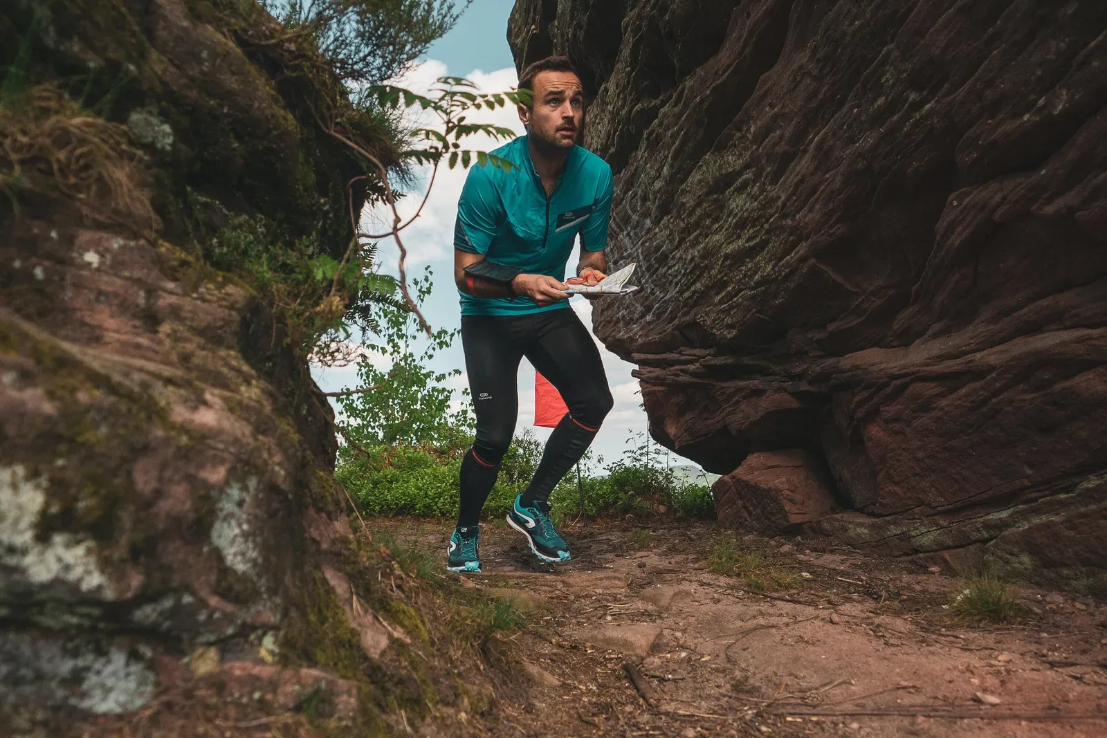 Walker holding a map while stepping through a narrow passage between red sandstone rocks