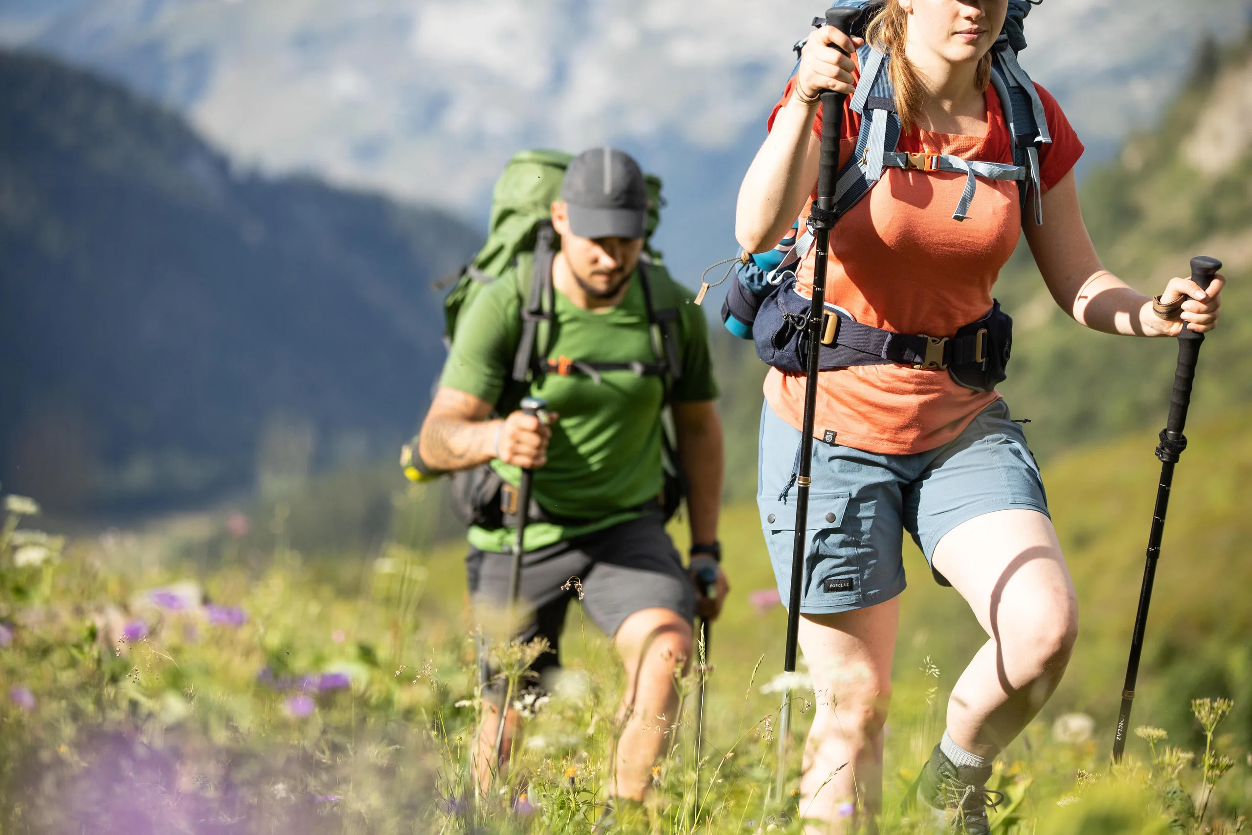 Two hikers in shorts and t-shirts with poles walking through a summer wildflower meadow