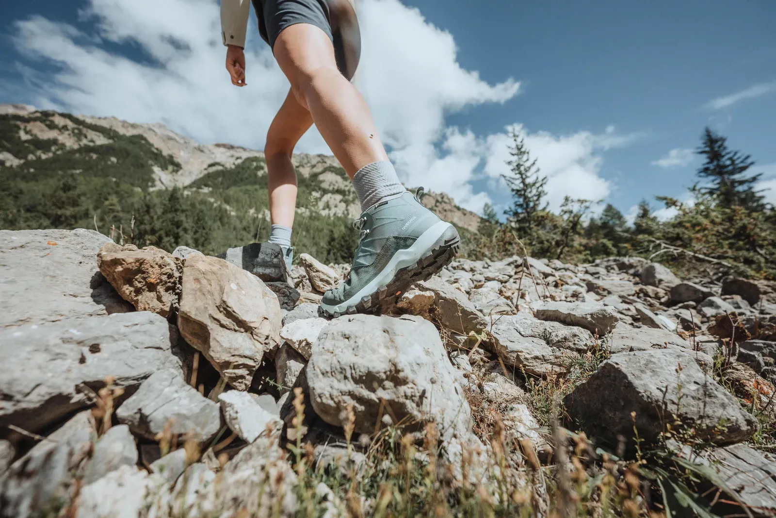 Close-up of a hiker in boots stepping across rocks on a sunny trail