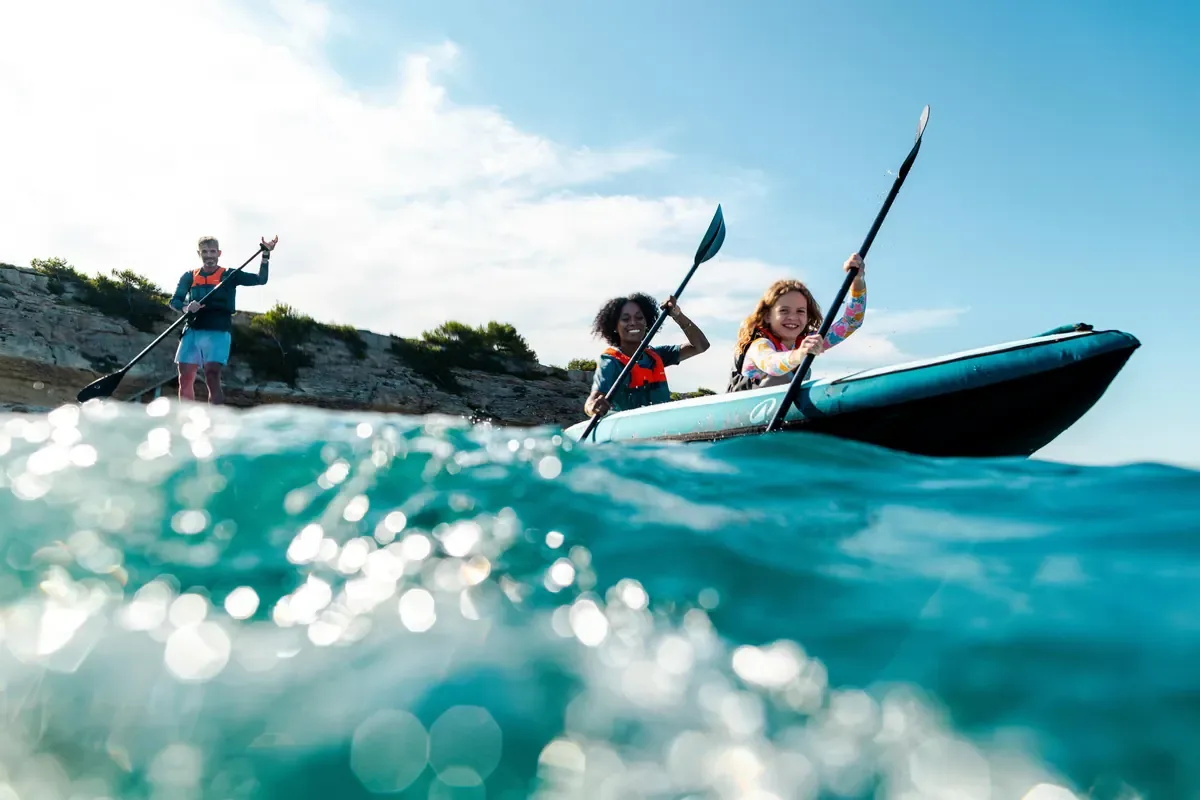 Kayakers paddling in clear turquoise water along a rocky shoreline