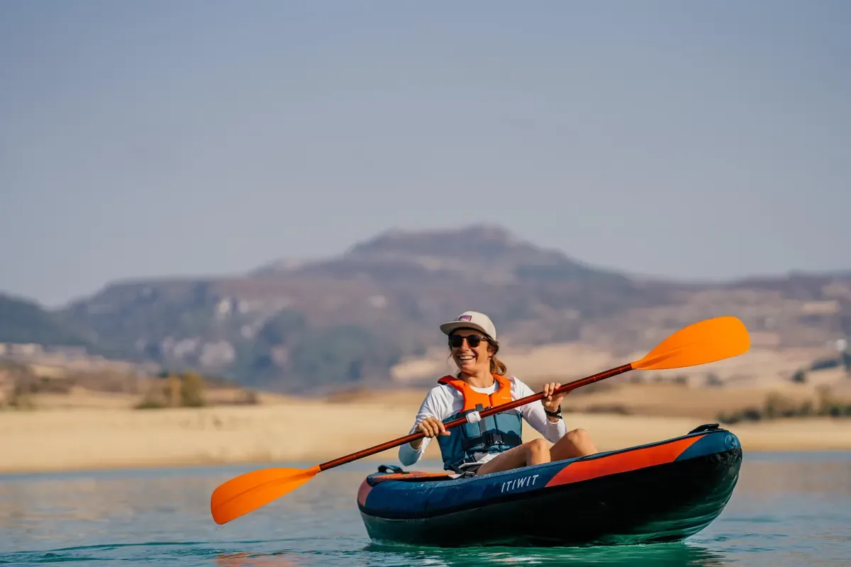 Smiling kayaker paddling clear blue water with dry sandy hills behind