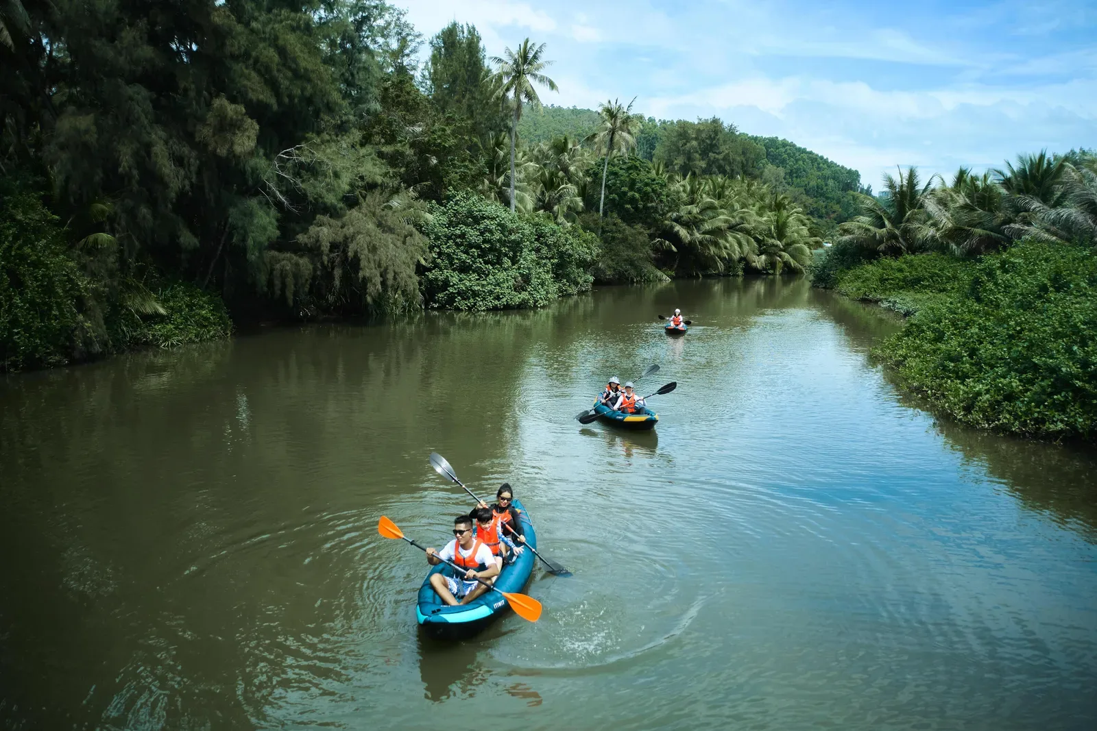 Kayakers paddling down a green tropical river lined with palms