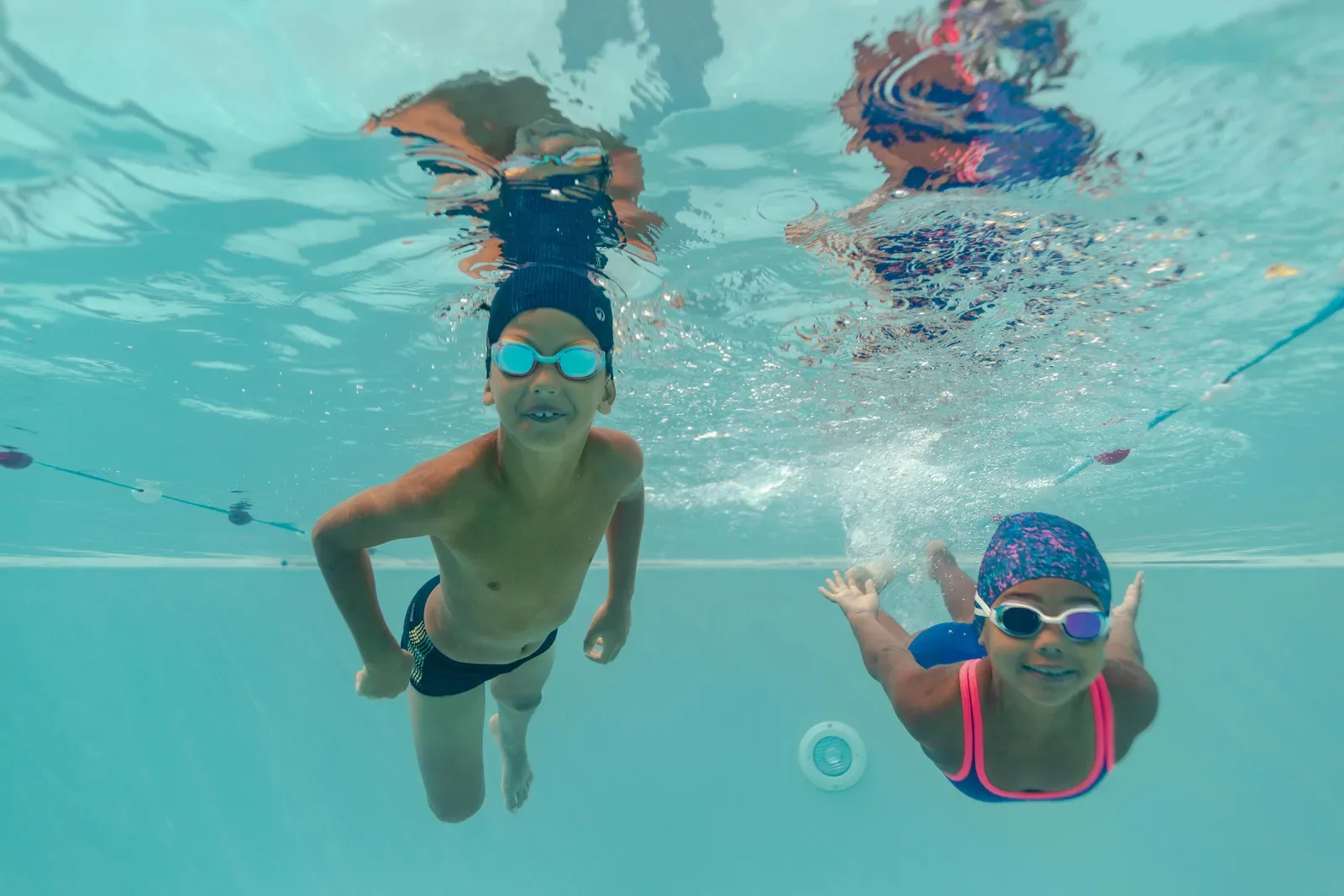 Two kids in goggles swimming underwater in a pool