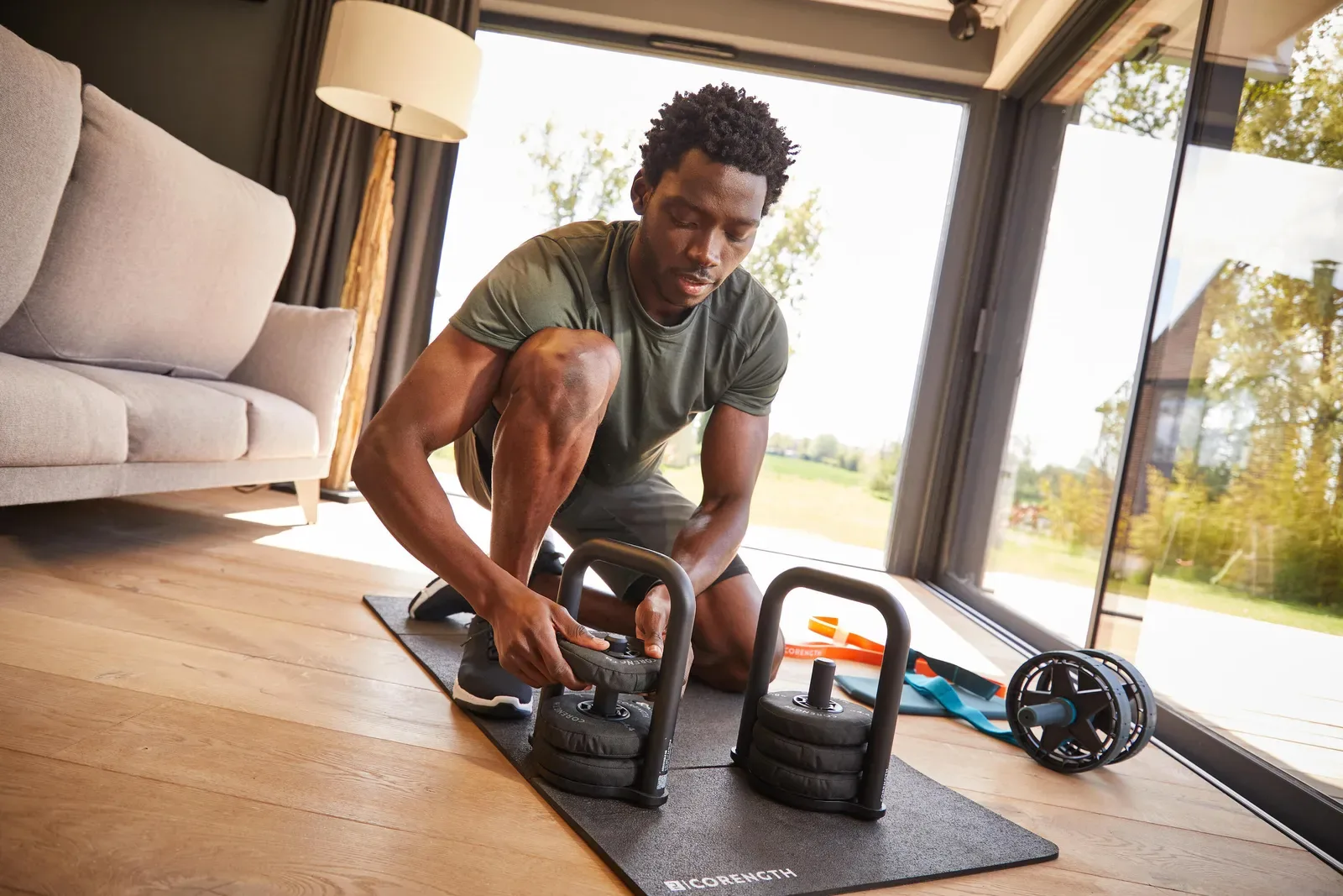 Man adjusting a pair of adjustable kettlebells on a mat at home