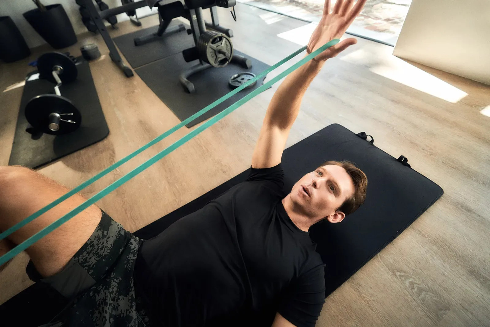 Man lying on an exercise mat stretching his leg with a resistance band