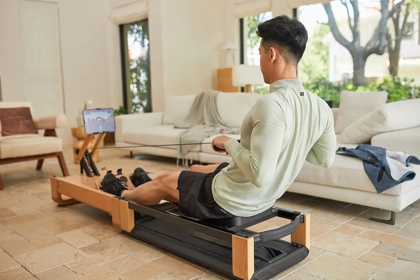 Man using a wooden rowing machine in his living room beside the sofa