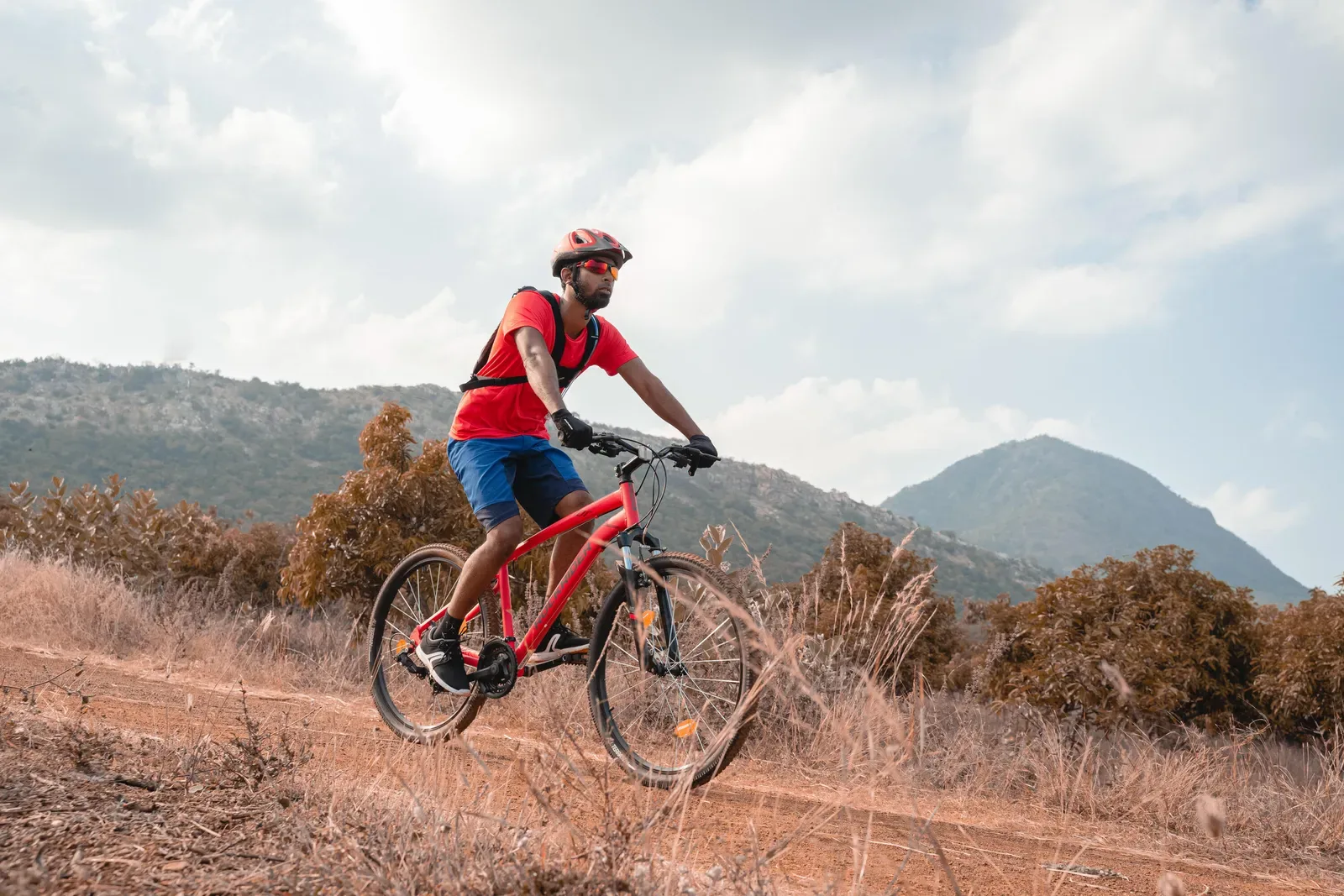 Mountain biker in a red helmet riding a dry dirt trail with hills behind