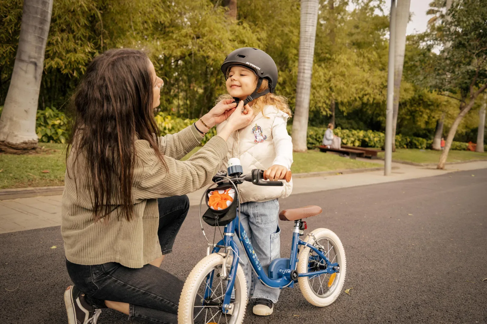 Mum fastening a toddler helmet beside a balance bike