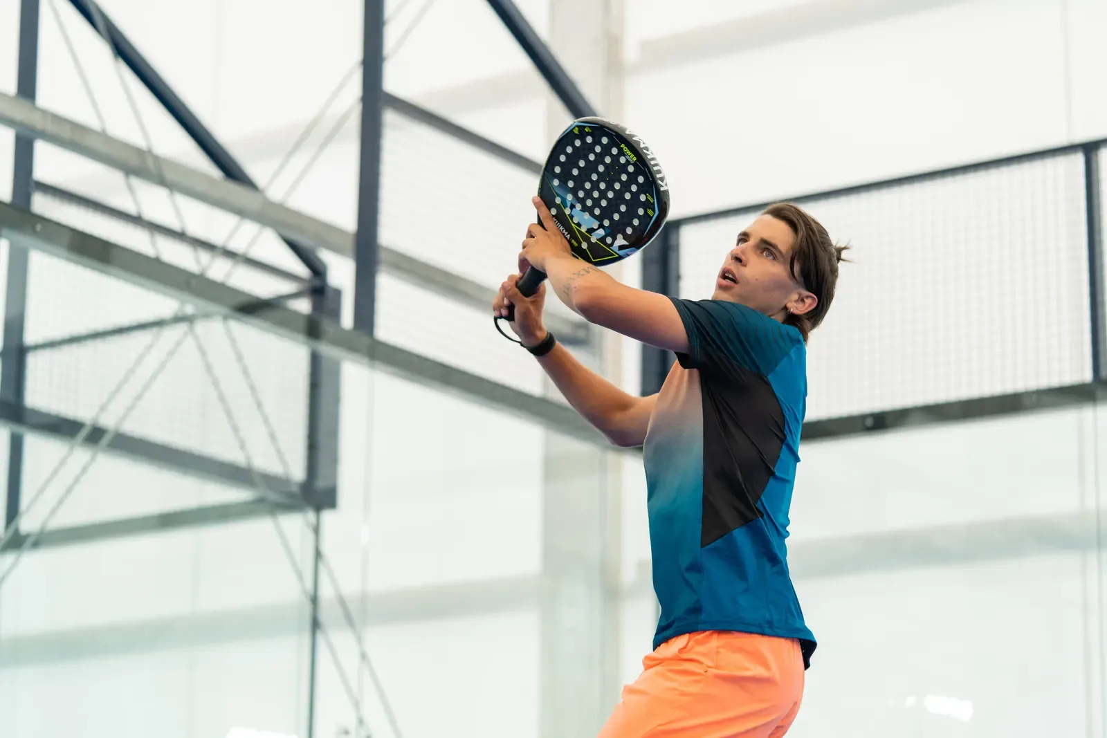 Padel player preparing a backhand volley beside the court mesh