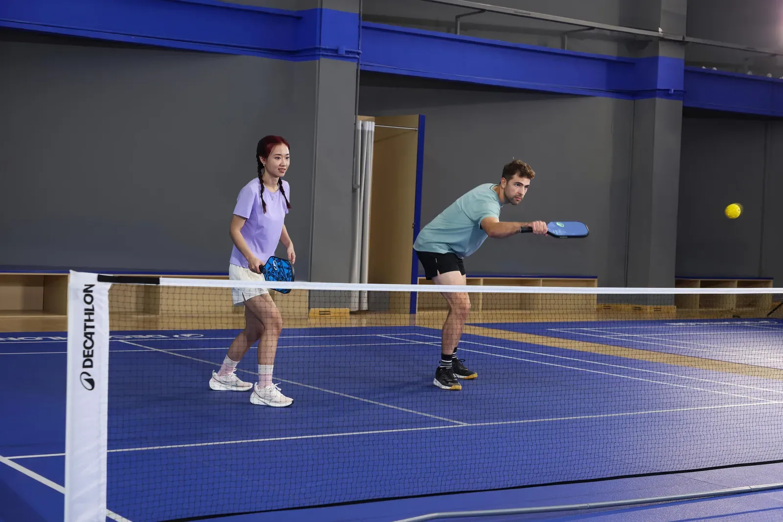 Man and woman playing a doubles rally of pickleball on an indoor court