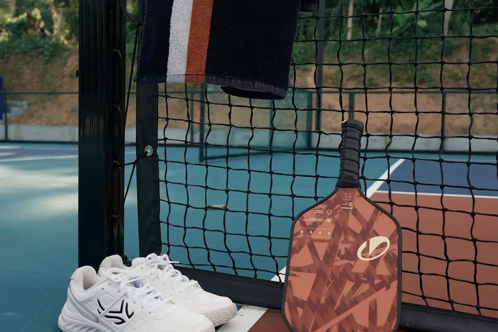 Pickleball paddle and court shoes resting at the net post with a towel hung above