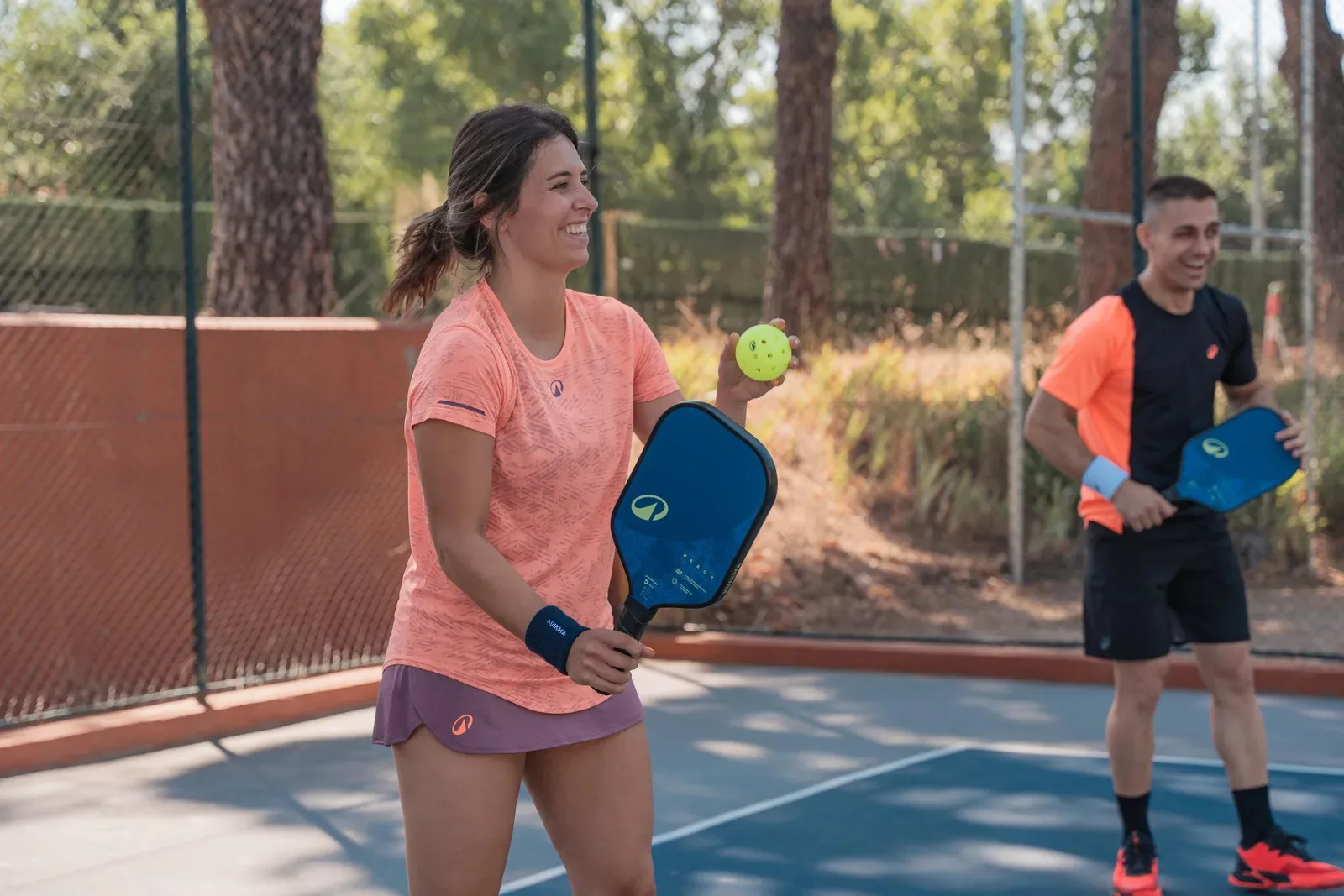 Smiling pickleball player ready with her paddle at the net, partner behind