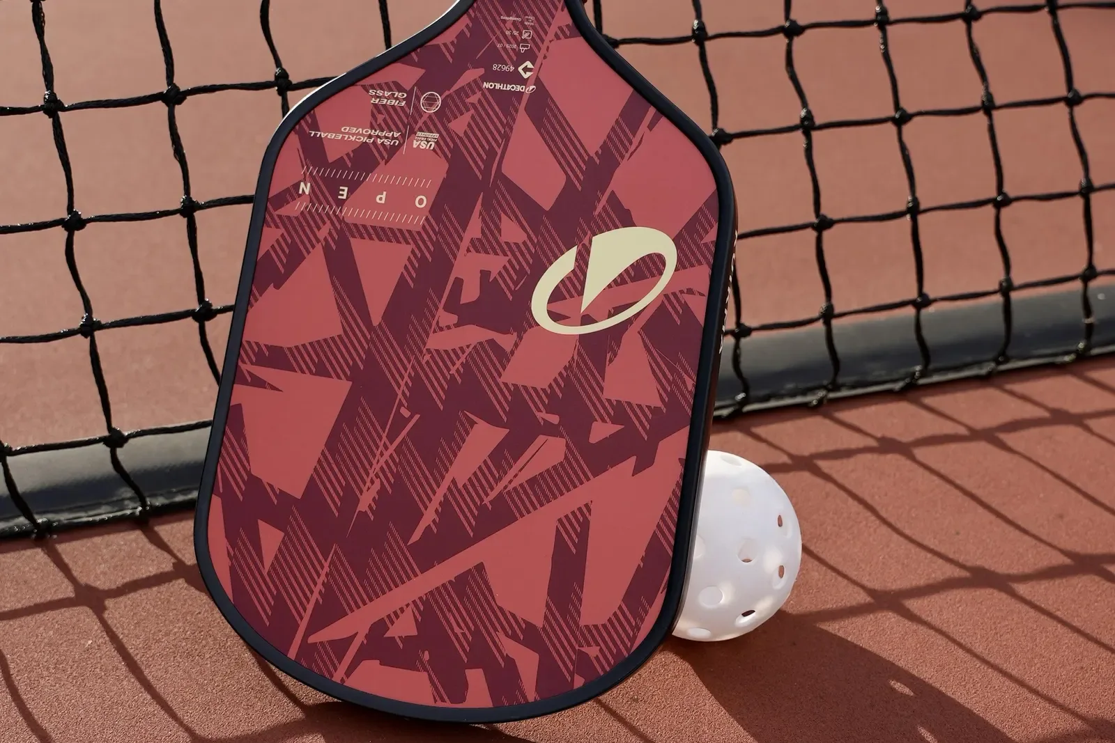 Red pickleball paddle and ball resting against the net on a court