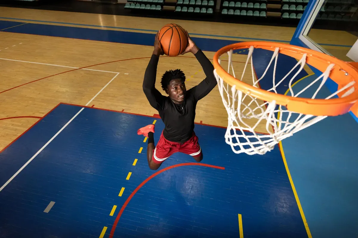 Player rising to dunk a basketball at an orange rim and white net