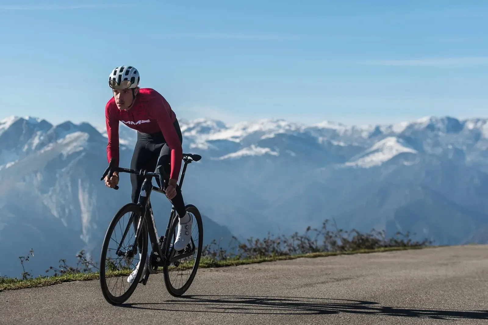 Road cyclist climbing a mountain road below snowy peaks