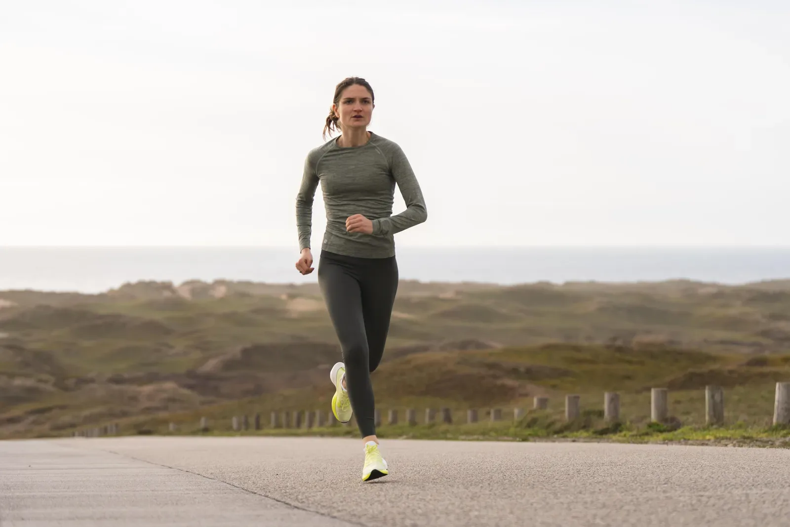 Woman running on a quiet road through low coastal heath with the sea on the horizon