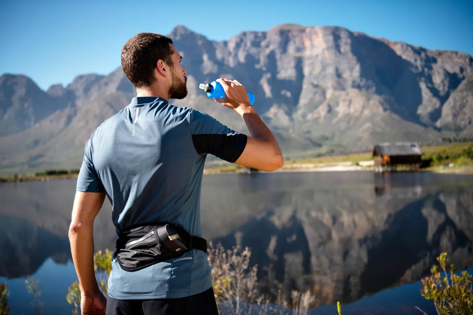Runner with a waist belt drinking from a soft flask beside a mountain lake