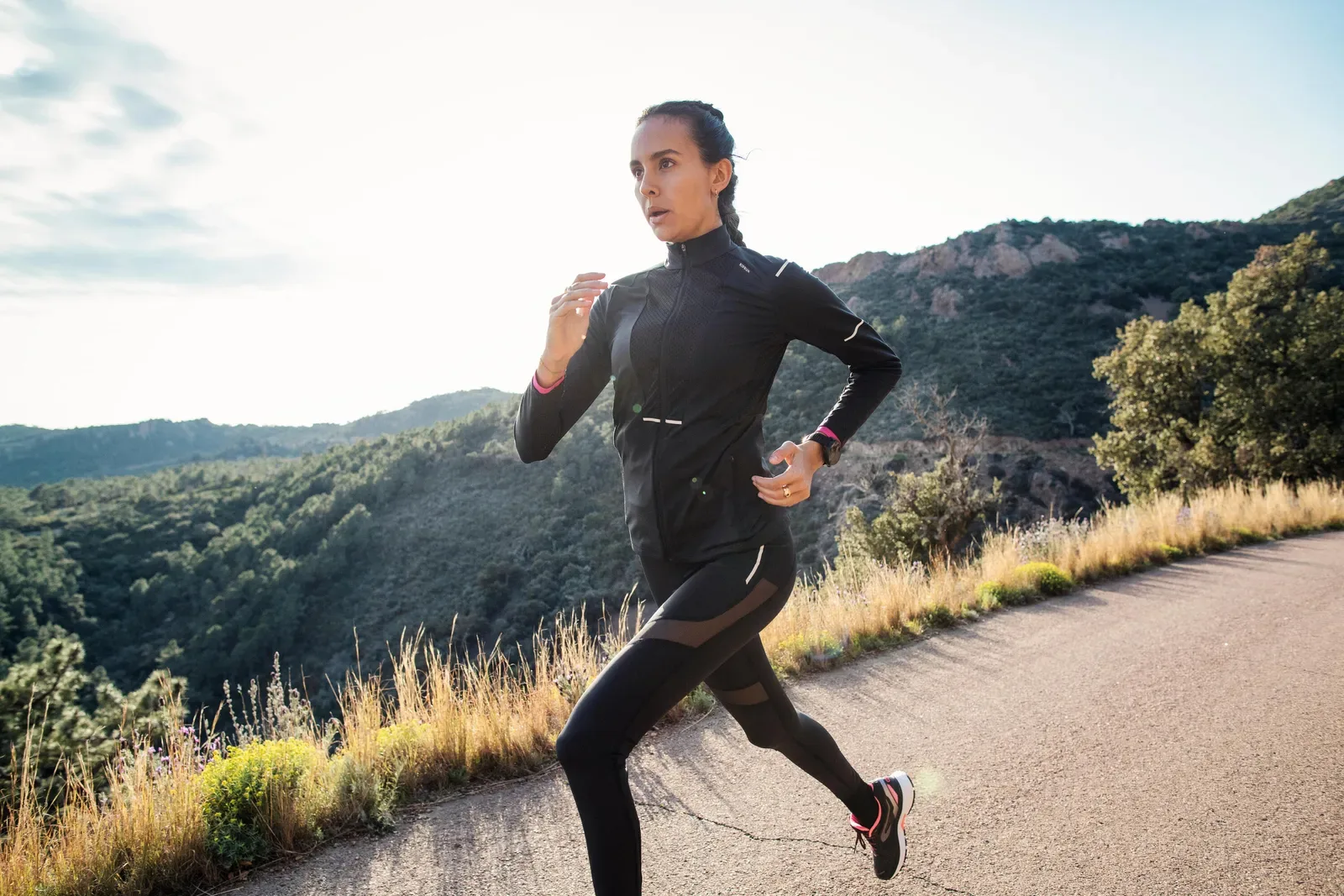 Woman running along a hillside path lined with golden grass and bushland