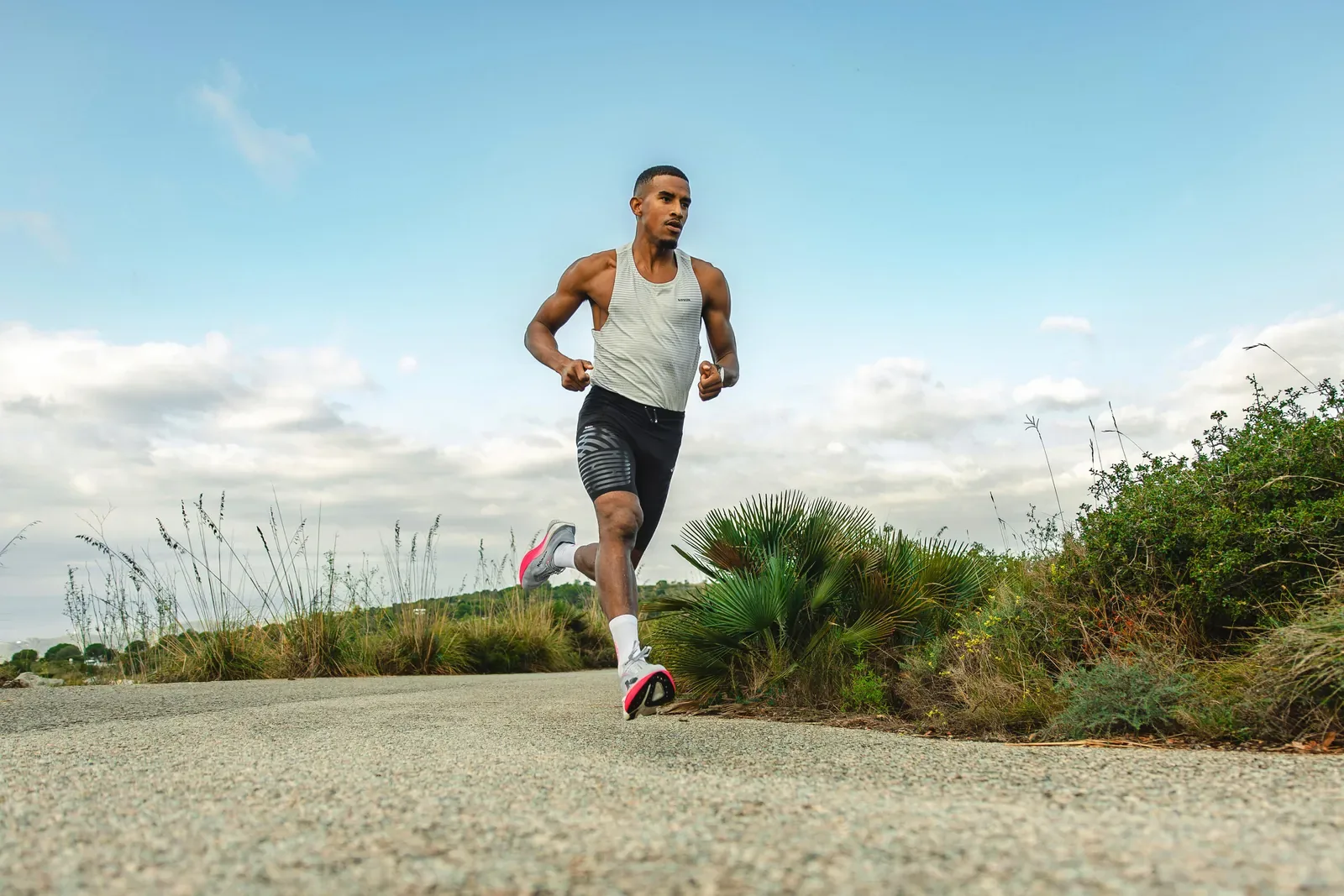 Man in a running singlet and shorts on a sunny road lined with low palms