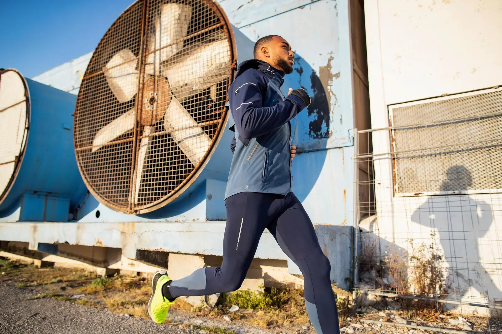 Runner in gloves, tights and a winter running jacket passing an old industrial wall