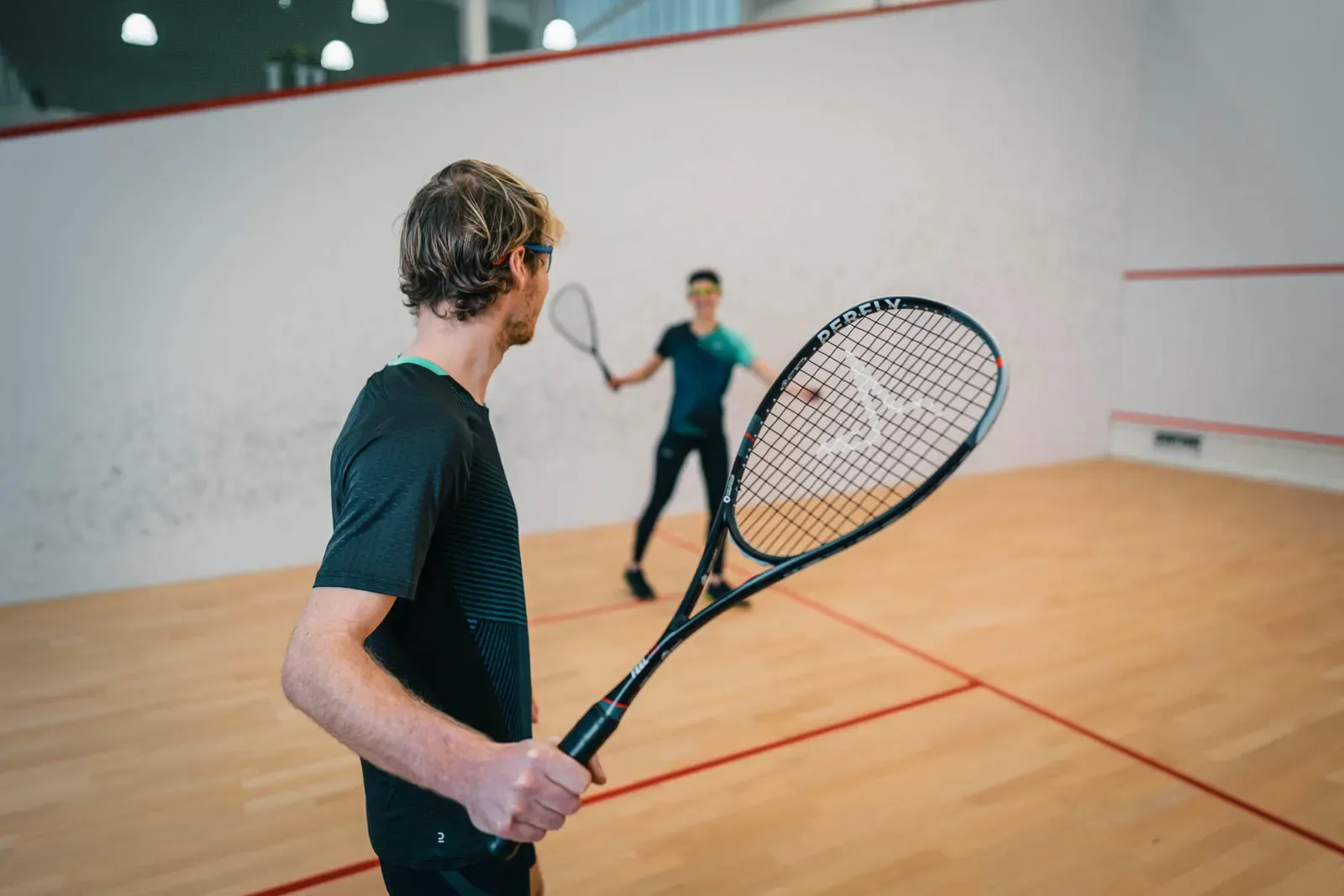 Squash player holding his racquet with a playing partner on court behind