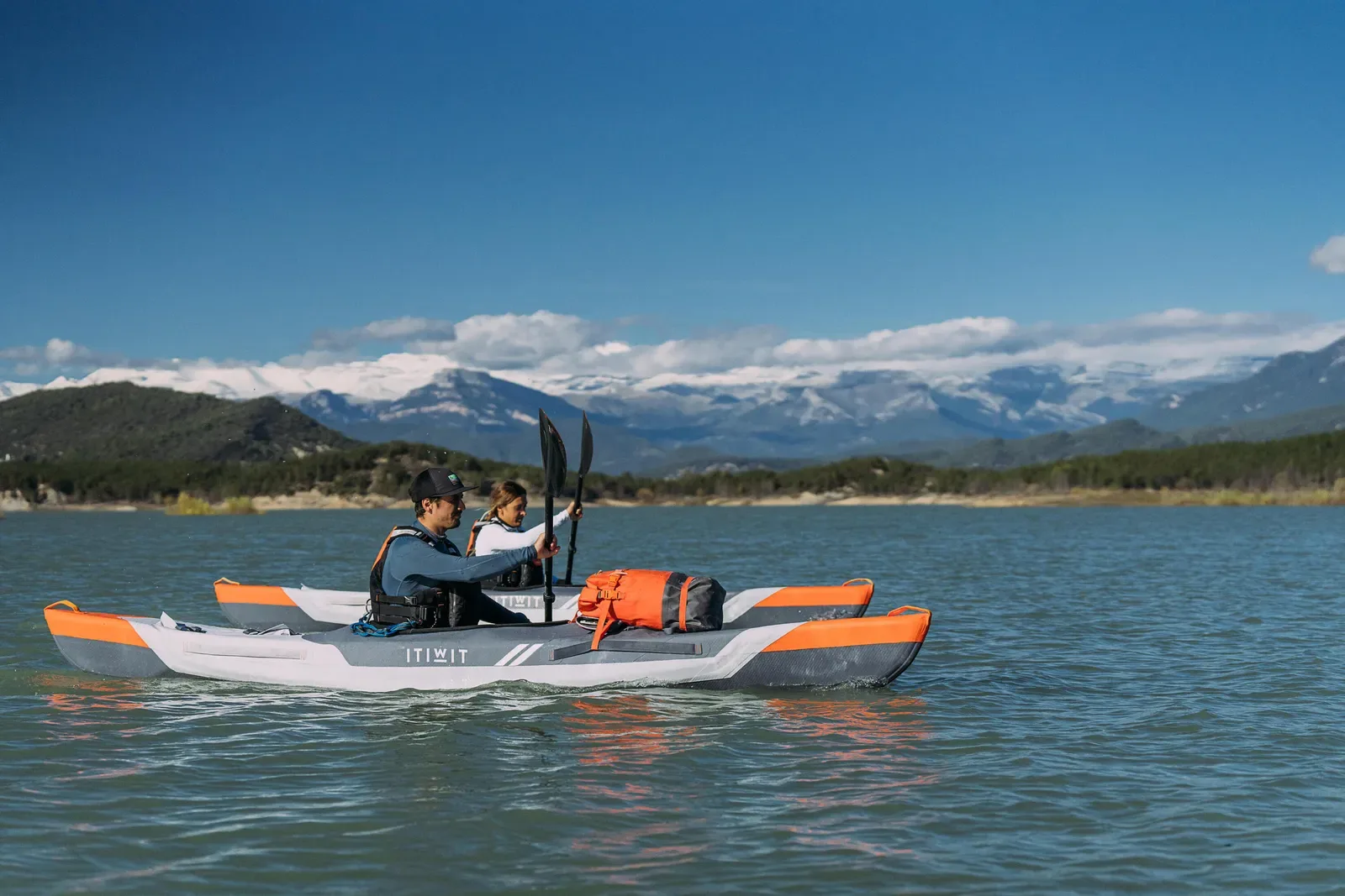 Two paddlers in a tandem kayak on a lake with snowy mountains behind
